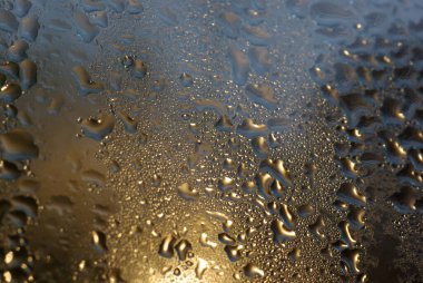 Şehir ışıklarıyla ıslak pencere camına su damlıyor.