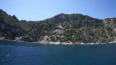 Kayalık bir deniz kıyısı ve beyaz bir tekne dalgalarda yüzüyor..