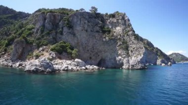 Kayalık bir deniz kıyısı ve beyaz bir tekne dalgalarda yüzüyor..