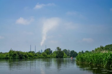 Ufuktaki uzun bir baca bir nehrin yanında, gökyüzüne doğru tütüyor..