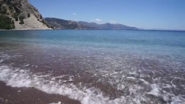 小石のビーチで純粋な透明海の波は 地平線上の山々 — ストック動画