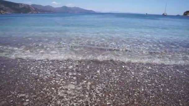 清澈清澈的大海冲刷着海滩上的卵石 地平线上的山脉和船只 — 图库视频影像