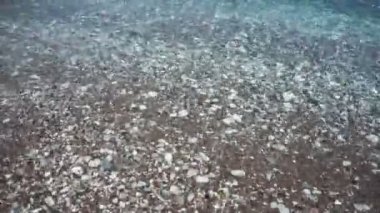 Çakıl taşlı sahilde şeffaf bir deniz dalgası..