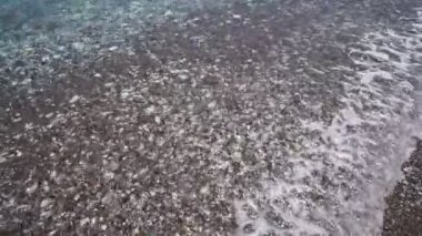 Çakıl taşlı sahilde şeffaf bir deniz dalgası..