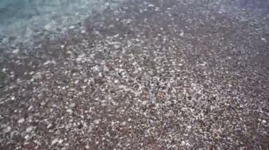 Çakıl taşlı sahilde şeffaf bir deniz dalgası..