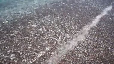 Çakıl taşlı sahilde şeffaf bir deniz dalgası..