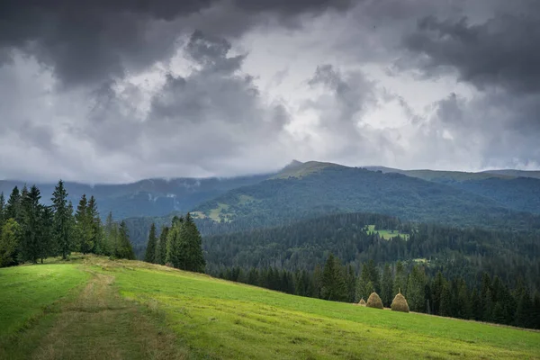 Çimleri biçilmiş dağ manzarası, saman yığınları ve kara yağmur bulutları