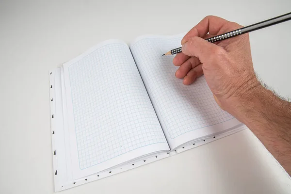 Male hand with a pencil writes in a checkered notebook sheet. Selective focus. Blurred background.