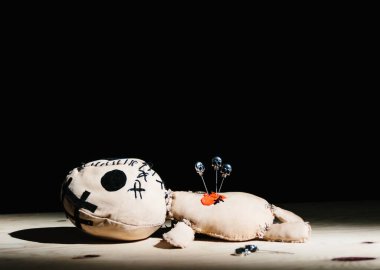 Sihirli ayinin için kara arka planda kafatasları olan iğneler vudu bebeğine saplanmış.