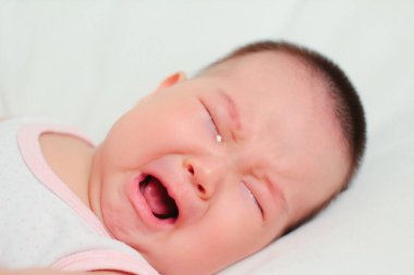 Bir yaşındaki Asyalı kızın yakın çekimi. Beyaz arka planda ağlayan bebek