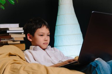 Bilgisayarlı Asyalı bir çocuğun portresi evde okuyor, uzaktan eğitim görüyor.
