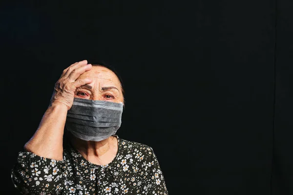 Portrait of an elderly woman in medical mask on a black background. Old people in risk zone because of virus epidemy, COVID-2019 pandemic