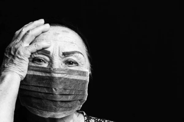 Close up black and white portrait of an elderly woman in medical mask on a black background. Old people in risk zone because of virus epidemy, COVID-2019 pandemic