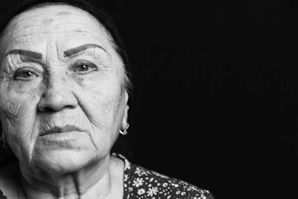 Black and white portrait on an old woman on a black background. Sad grandmother