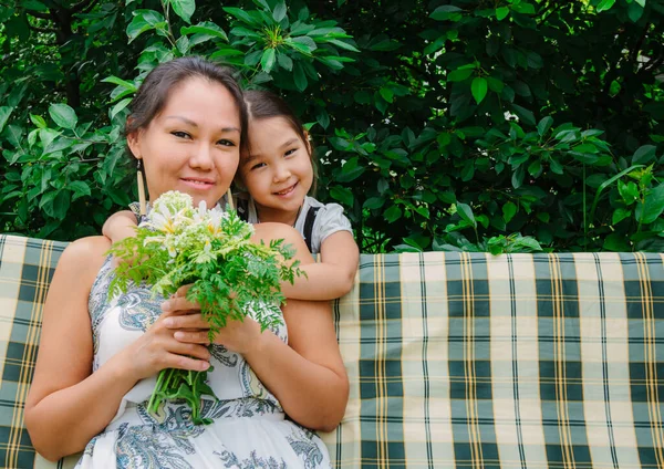 Sweet family moments, portrait of a little Asian girl giving flowers to her mom, congratulating with Mother's Day, happy mood, green colors, tone