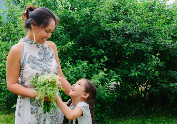 Sweet family moments, portrait of a little Asian girl giving flowers to her mom, congratulating with Mother\'s Day, happy mood, green colors, tone