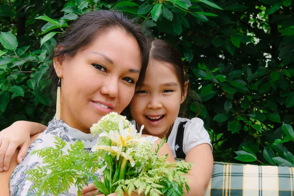 Sweet family moments, portrait of a little Asian girl giving flowers to her mom, congratulating with Mother\'s Day, happy mood, green colors, tone