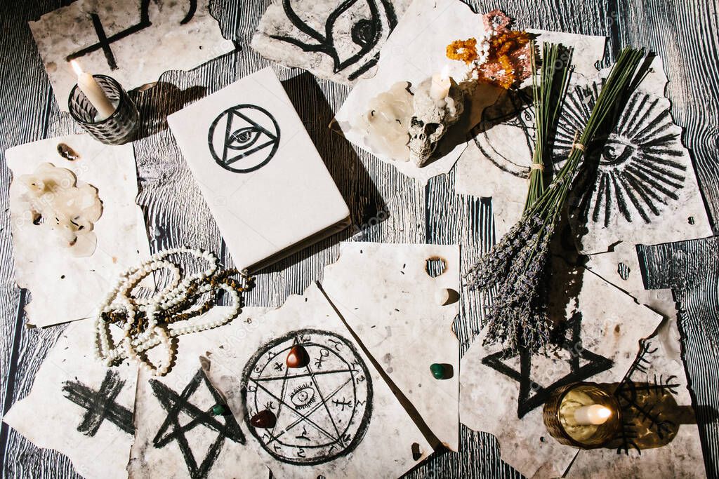 White magic book laying on the table with old manuscripts with occult symbols, candles, lavender. Concept of fortune telling, ritual, altar, spiritism, secret knowledge