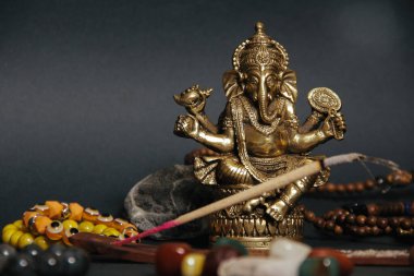 Siyah arka planda esrarengiz semboller. Aroma çubuğu, Ganesha biblosu, taş tespih. Üst görünüm