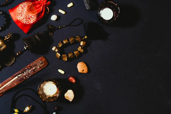 Occult symbols laid out on a black background. Aroma stick, Buddha figurine, stone rosary. Top view