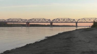 Yük treni akşam günbatımında Sibirya'da Nehri geçip köprüde. renk düzeltme olmadan video