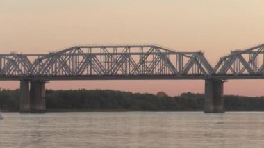 Yük treni akşam günbatımında Sibirya'da Nehri geçip köprüde. renk düzeltme olmadan video