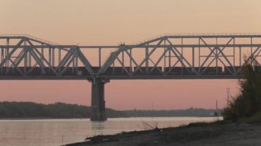 Yük treni akşam günbatımında Sibirya'da Nehri geçip köprüde. renk düzeltme olmadan video