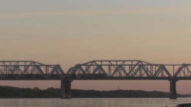 Yük treni akşam günbatımında Sibirya'da Nehri geçip köprüde. renk düzeltme olmadan video