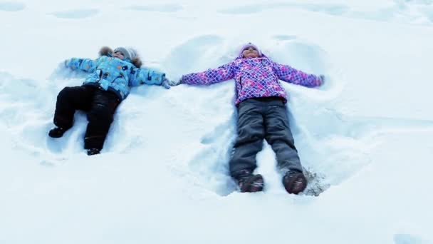 Starsza siostra i brat, leżącego w śniegu i zrobić aniołów w Wigilię Bożego Narodzenia. zwolnionym tempie — Wideo stockowe