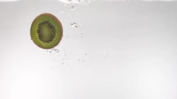 Skivor av Kiwi faller sakta ner i det klara vattnet på en vit bakgrund — Stockvideo