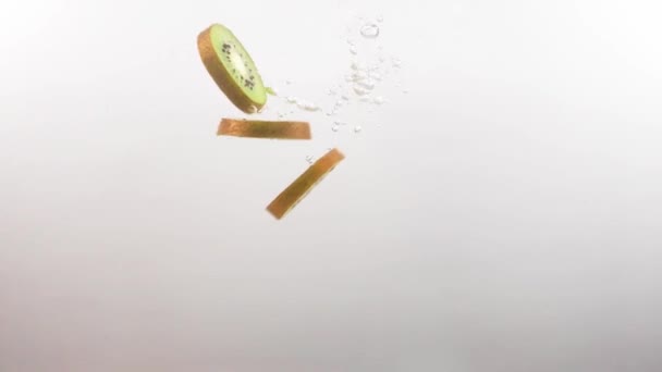 Sneetjes Kiwi fruit vallen langzaam in het heldere water op een witte achtergrond — Stockvideo