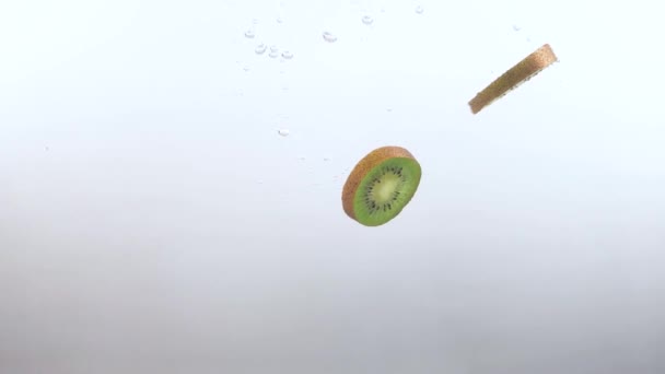 Sneetjes Kiwi fruit vallen langzaam in het heldere water op een witte achtergrond — Stockvideo