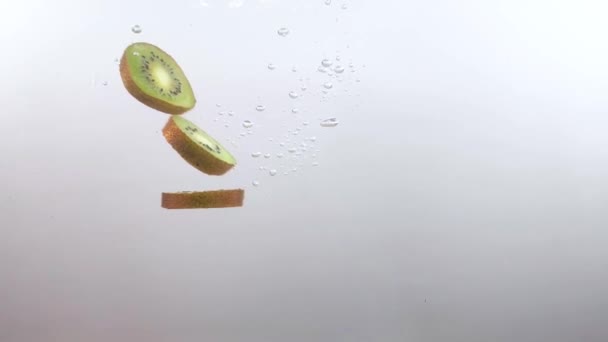 Plasterki owoców kiwi powoli wpadają do jasnej wody na białym tle — Wideo stockowe
