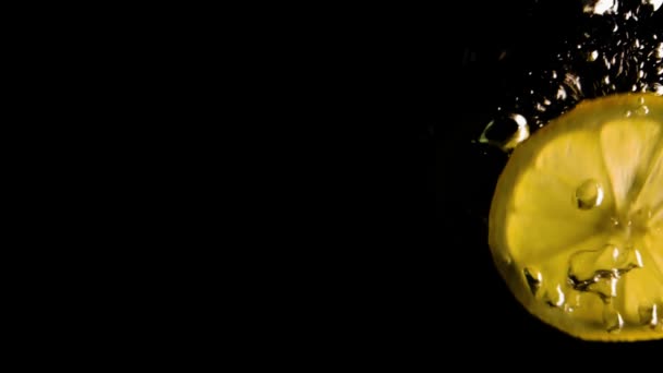 Zitrone fällt vor schwarzem Hintergrund ins Wasser. Zeitlupe — Stockvideo