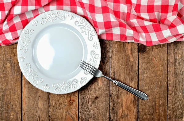 Dekoratif seramik tabak, çatal, halka ve kırmızı kareli masa örtüsü eski vintage ahşap masa arka plan üzerinde beyaz - yukarıdan görüntüleyin — Stok fotoğraf