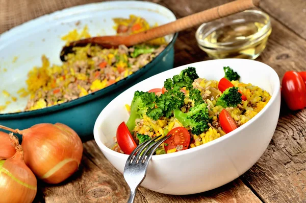 Nahaufnahme von Gabel und Thunfisch-Risotto mit Gemüse, Tomaten, Brokkoli und Petersilie in der Schüssel, Zwiebeln, Öl und Pfanne im Hintergrund — Stockfoto