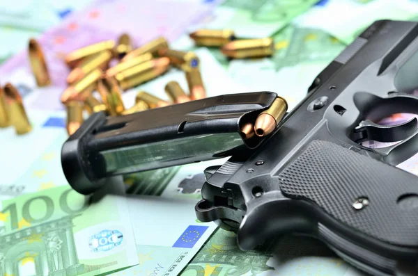 Крупный план пистолета, заряженного магазина и пуль на фоне банкнот евро — стоковое фото