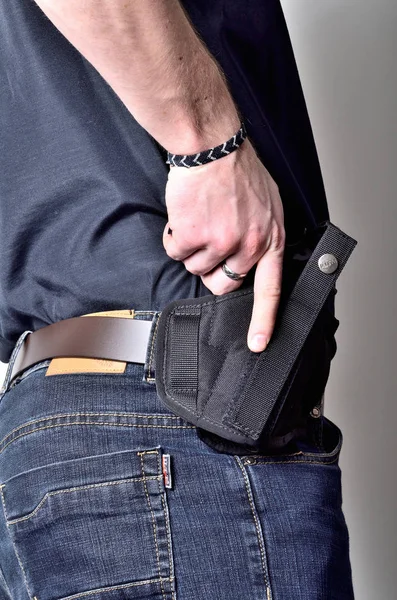 Homme tirant un pistolet de l'étui à ceinture, jeans bleus, chemise noire — Photo