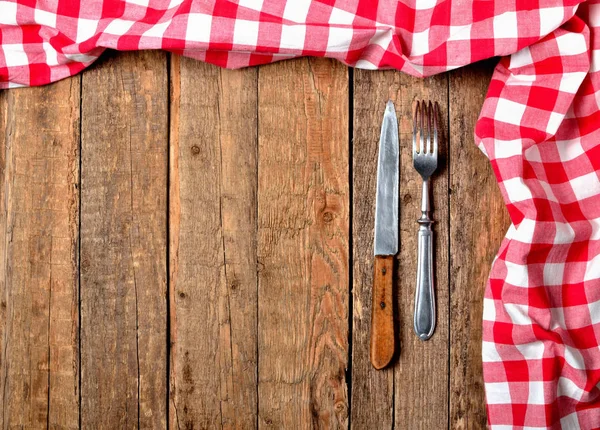 Kırmızı kareli masa örtüsü üst ve sağ çerçevedeki, bıçak ve çatal vintage ahşap masa arka plan üzerinde-görüntülemek yukarıdan — Stok fotoğraf