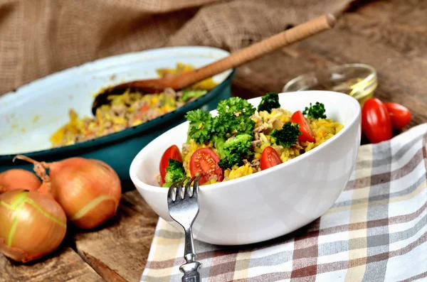 Gabel und Thunfisch-Risotto mit Gemüse, Tomaten, Brokkoli und Petersilie in der Schüssel, Zwiebeln, Öl und Pfanne im Hintergrund — Stockfoto