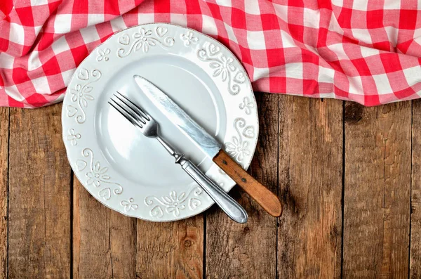 Boş dekoratif tabak ve eski vintage ahşap üst tarafında kırmızı kareli masa örtüsü masa arka plan - yukarıdan görüntüleyin bıçak ve çatal — Stok fotoğraf