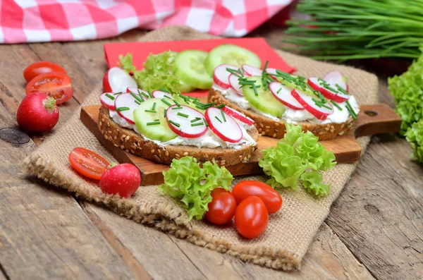 Зерновой хлеб со спредом, свежая редиска, огурец и помидоры - концепция здорового фитнес-завтрака или закуски, свежий салат и лук на заднем плане — стоковое фото