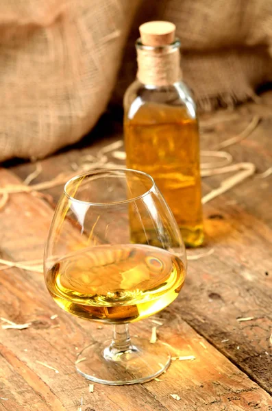 Gelas cognac pada latar belakang kayu pedesaan dan botol di foto vertikal latar belakang — Stok Foto