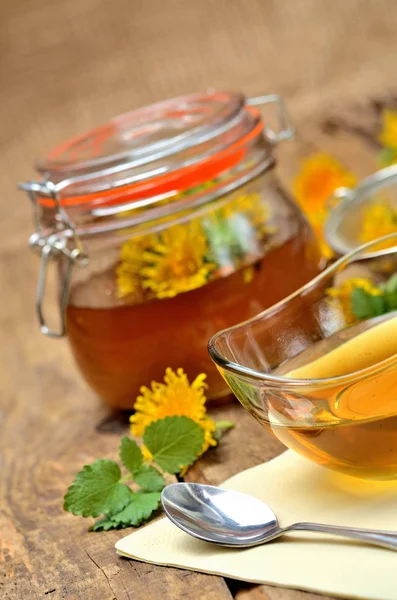 Close-up of dandelion honey, spoon, dandelion head around and full jar in background - vertical photo — Stock Photo, Image