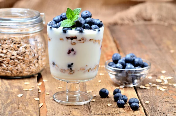 Griechischer Joghurt mit Haferflocken, frischen Blaubeeren und Minzblättern, im Hintergrund ein Glas Haferflocken — Stockfoto