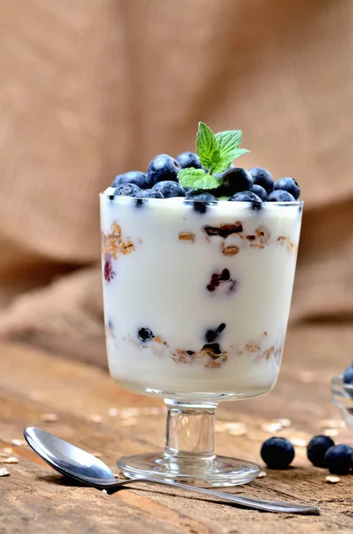 Joghurt mit Haferflocken, frischen Blaubeeren und Minzblättern und einem Löffel im Hintergrund — Stockfoto