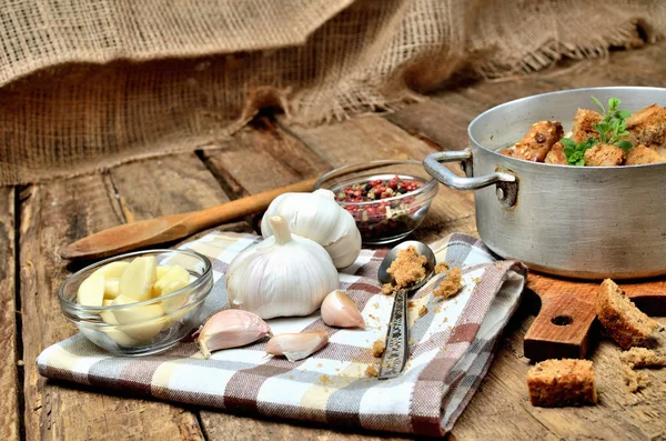 Zbliżenie Zupa czosnkowa w starym garnku, świeżego czosnku cebule, ząbki, kolorowy pieprz, drewnianą łyżką, grzankami i ręcznik na rustykalne drewnianym stole — Zdjęcie stockowe