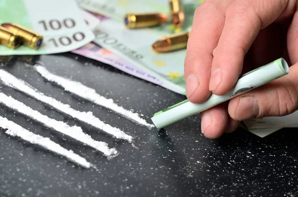 Hand of man snorting cocaine, euro banknotes and gun ammunition in background — Stock Photo, Image
