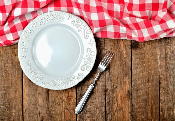 Dekoratif seramik tabak, çatal, halka ve eski vintage ahşap masa arka plan - üstten görünüm üst tarafında kırmızı kareli masa örtüsü — Stok fotoğraf