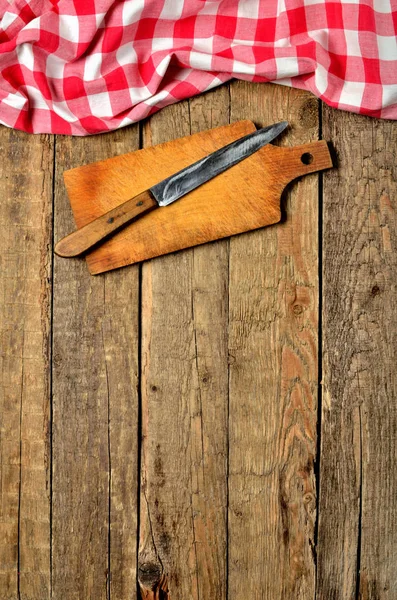 Μαχαίρι σε ξύλο κοπής και ένα κόκκινο καρώ τραπεζομάντιλο επάνω πλαίσιο σε ξύλινο τραπέζι φόντο - κάθετη φωτογραφία — Φωτογραφία Αρχείου